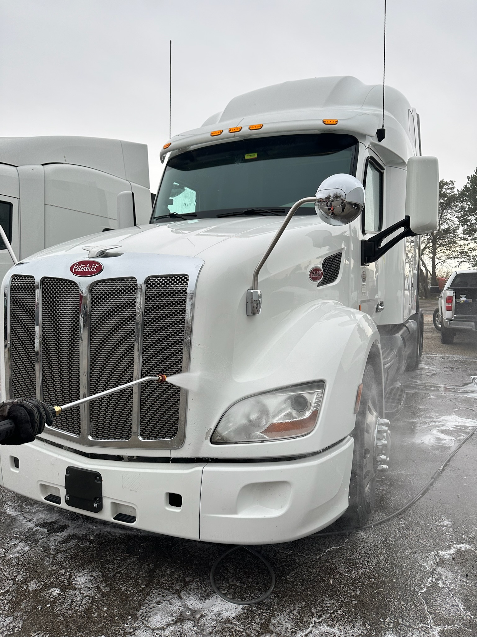 A white Peterbilt semi-truck being washed with a spray nozzle